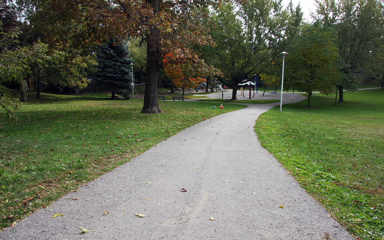 A paved pathway in Cassels Avenue Playground leading to the splash pad and swings.