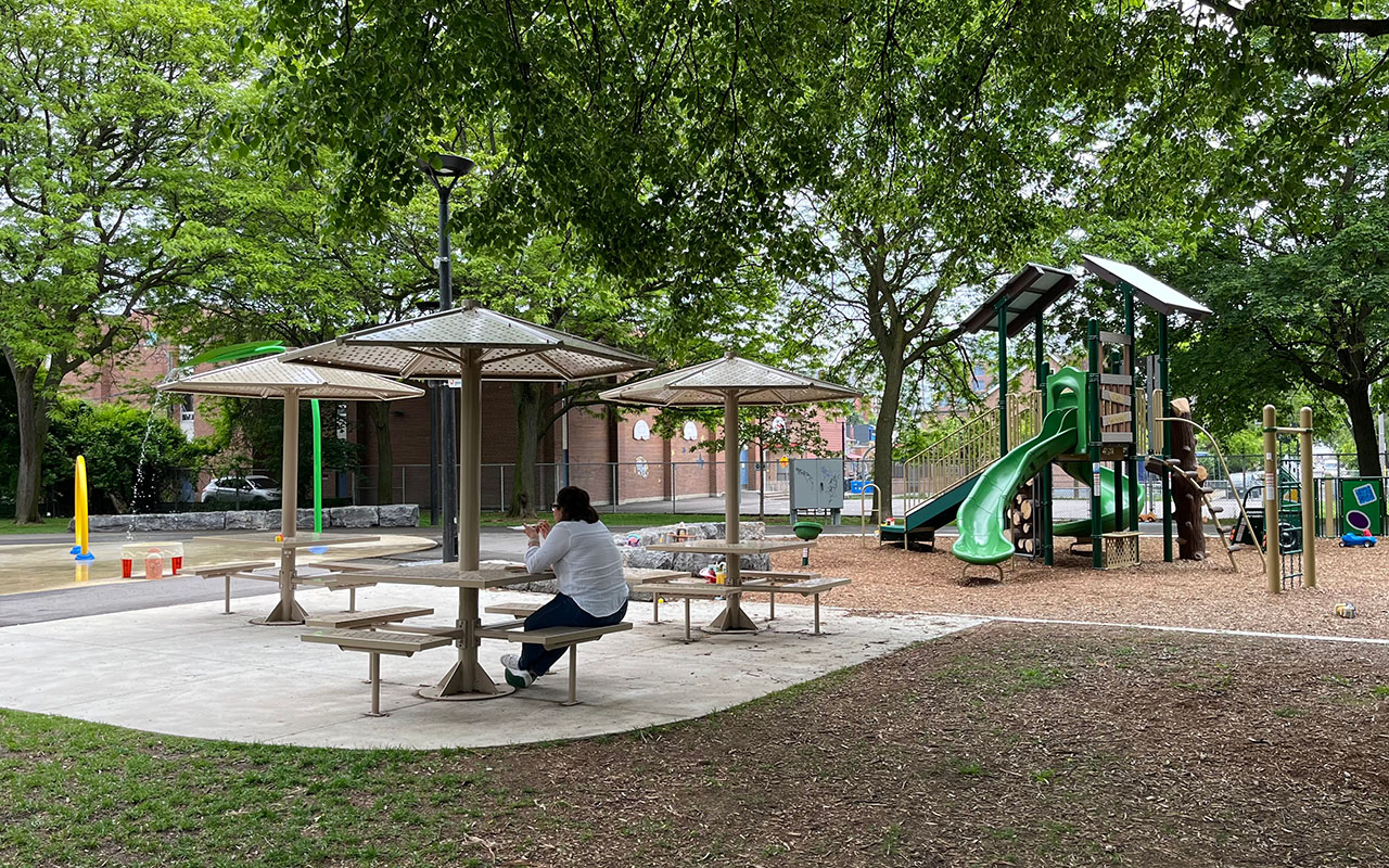 Shaded picnic tables by the splashpad and children's playground at Osler Playground.