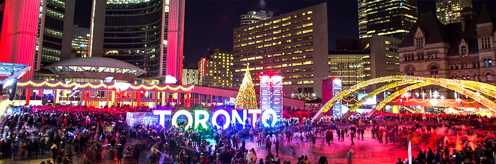 Photo of Nathan Phillips Square at night in the winter. People skating in front of the Toronto sign.