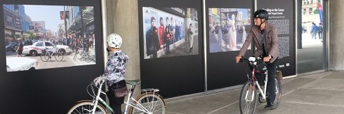 Two people on bicycles looking at a photo exhibition at City Hall regarding the intersection at Yonge and Dundas