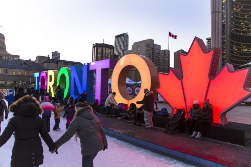 people skate in front of an illuminated Toronto sign