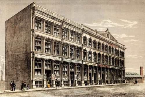 This hand-coloured newspaper print shows a three-storey block of buildings. The first storey is extra high, and has large, arched display windows. The names of stores and businesses are on signs across the front of the building, and on placards at eye level near the doors. At the top of the building on the right-hand side, a triangular roof ornament reads Phoenix Block 1872