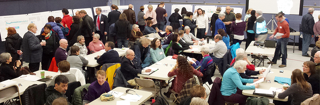 people seated at tables and standing while looking at the first community consultation presentation materials