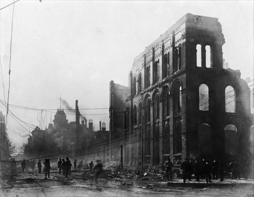 Front Street is lined with ruins, and the street is clogged with rubble and fallen hydro telegraph wires. Many people are viewing the ruins.