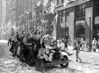 Cheering people sit in and on a car, waving flags