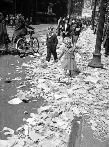 A small girl wades through drifts of tickertape and paper on the street.