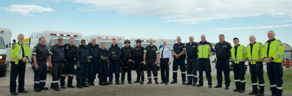 A row 19 members of Toronto Paramedic Services Special Teams pose in front of ambulances