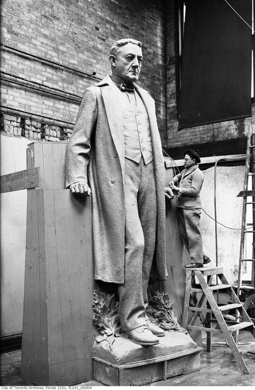 Large stone sculpture of a man in a long coat.