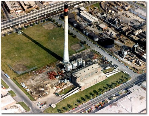 Large red brick building with a very tall concrete smokestack.