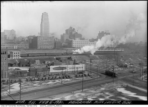 A billboard, trains, and the tall buildings of the city beyond.