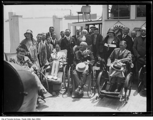 Group of men in wheelchairs or standing on the deck of a ferry boat.