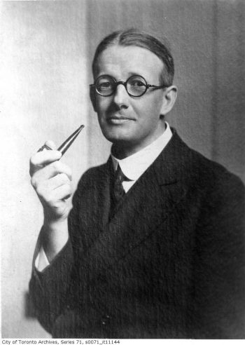 Man with round glasses, holding pipe.