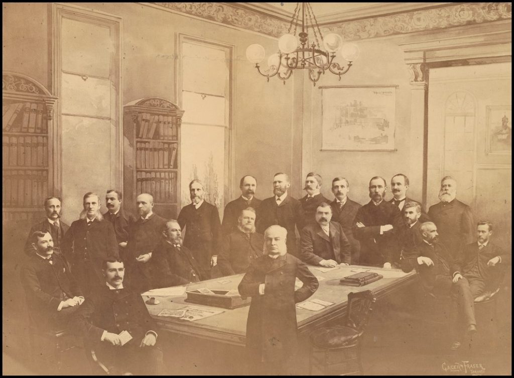 Men in dark suits standing around a table.