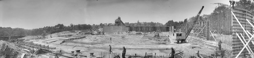 Workers and a crane erect semicircular forms on bare earth.