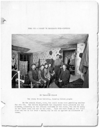 Page of book with photograph showing six men sitting on beds in small, low-ceilinged bedroom.