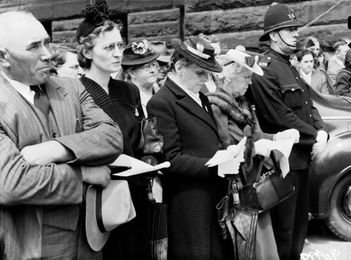 A group of men and women is standing outside, with the wall of Old City Hall visible behind them. A policeman in uniform is standing with the crowd.