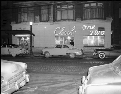 Cars parked in front of a wide building with "Club One Two" spelled out in lights on the front.