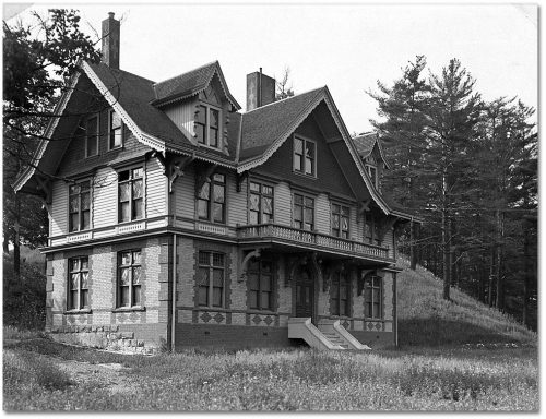 Three-storey building with decorative two-colour brick and peaked roof and eaves.