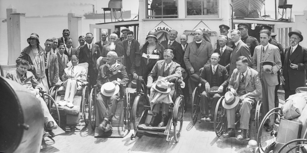 Group of men in wheelchairs or standing on the deck of a ferry boat.