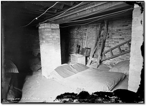 A mattress lies on the floor in an unfinished brick basement.