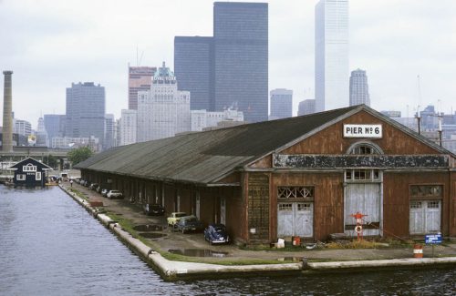 A long, low building extending out into the water, with the city behind it.