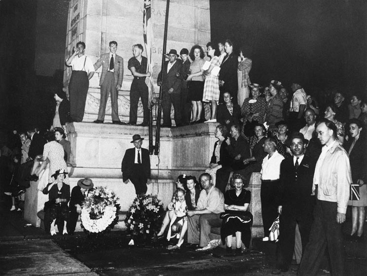 People stand and sit on and around the Cenotaph.