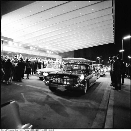 Large cars pull up under a broad illuminated awning.