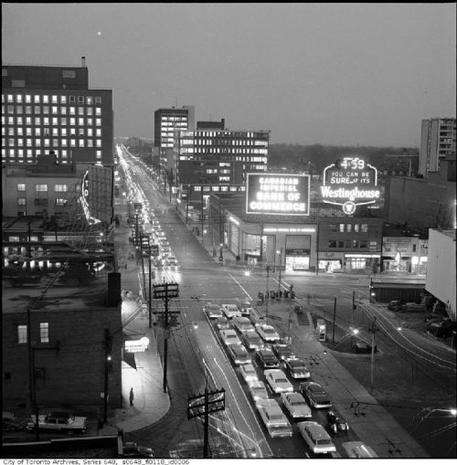 Illuminated office buildings, neon signs, and lines of cars with their headlights on.