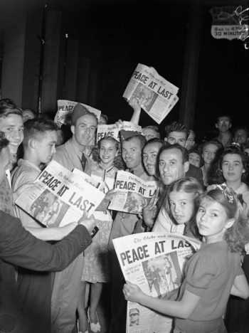 People read and hold up newspapers with the headline PEACE AT LAST.