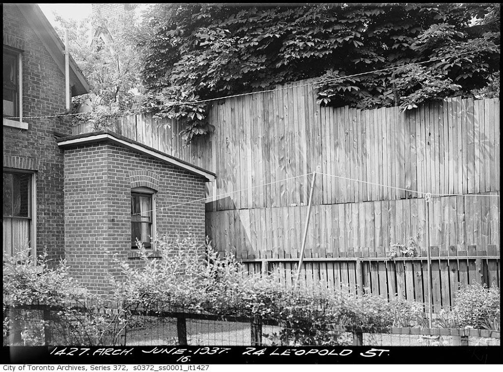 A wooden fence is almost as tall as the house beside it