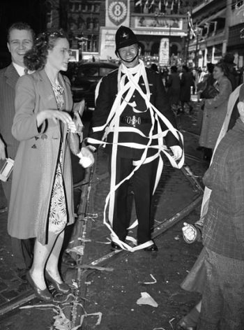 A grinning police officer is draped with streamers