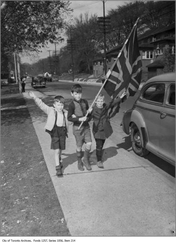 Small boys walk down a sidewalk, waving a Union Jack.