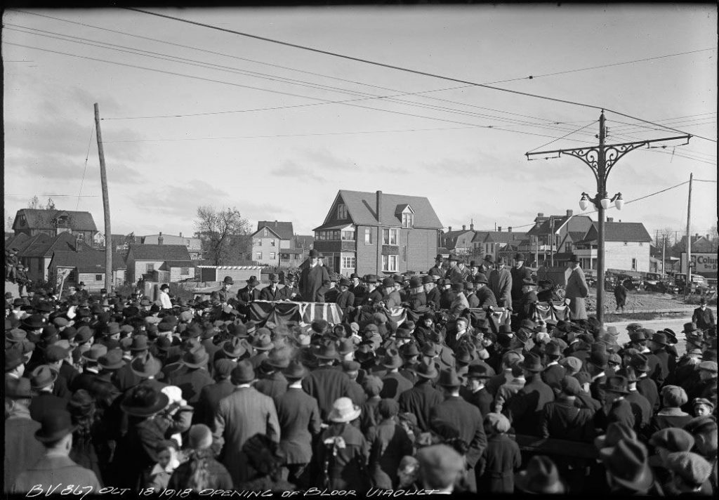 Crowd gathered around platform draped with flag.