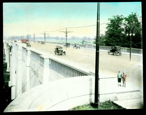 Cars driving on roadbed of viaduct, with two children in foreground.