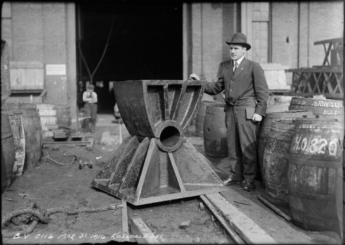 Man standing beside cast iron piece shaped like an hourglass coming up to his chest.