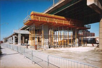 Bright yellow metal support structure and concrete forms under expressway deck