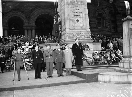 Group of men in armed forces uniforms standing in front of a stone pillar.