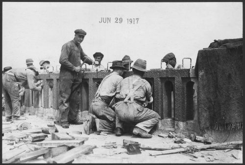 Men kneeling down to work on wasit-height concrete railing.