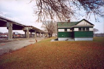 Looking past small wooden green and white park building to half-dismantled elevated expressway