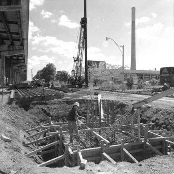 Worker guides concrete pouring into a concrete form in a hole in the ground