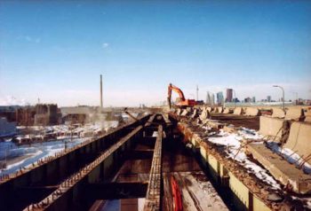 Large machine hammers away concrete on bed of raised expressway, leaving only metal support beams