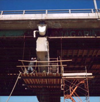 Worker standing on scaffold repairs old concrete support pillar