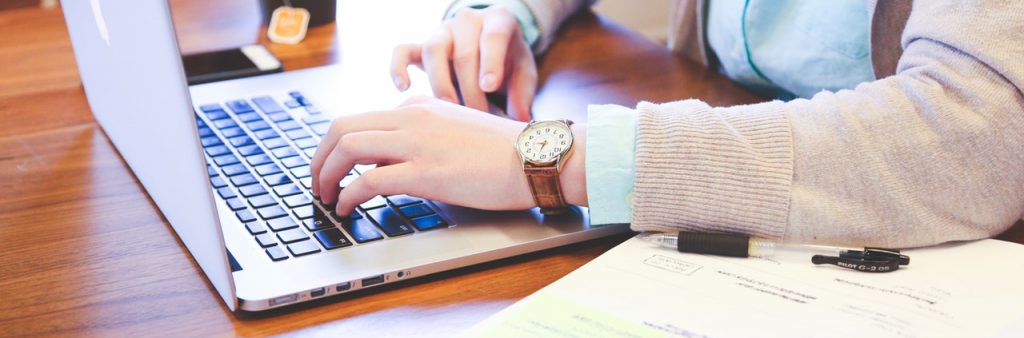 Person typing on laptop with open textbook