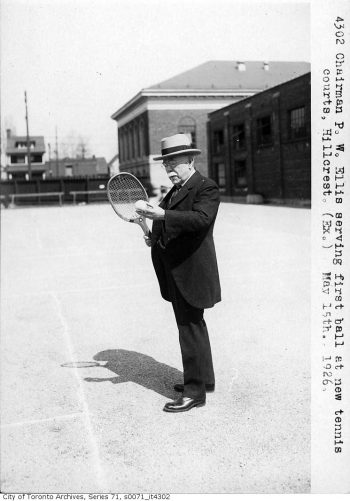 Man in suit holding tennis raquet.