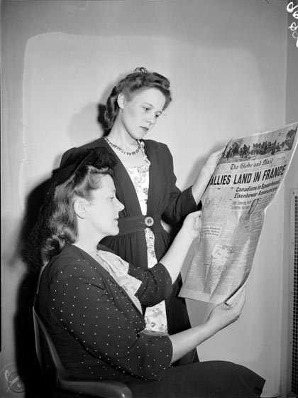 Two women look at an edition of the Globe and Mail. The headline reads, ''Alllies land in France: Canadians in spearhead, Eisenhower announces.'