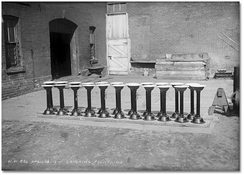 A row of freestanding cast-iron fountains, about three feet high, with white basins at the top.