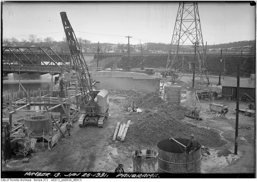 Construction on a pier in a river, with a steel bridge in the background.