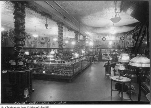 Store interior with wooden and glass cases, and many ceiling and floor lamps.