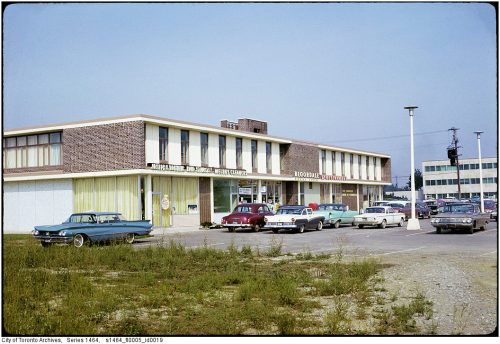 Cars parked in front of a two-storey strip mall with offices on the top floor.