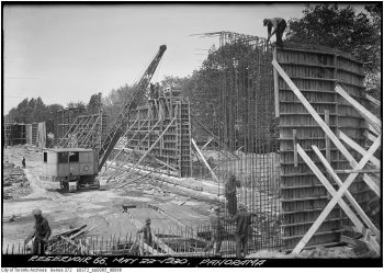 Workers and a crane erect a two-storey-high rebar form for concrete.